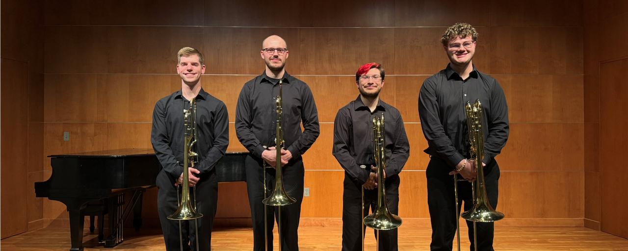 Four trombone students posing with trombones on stage.